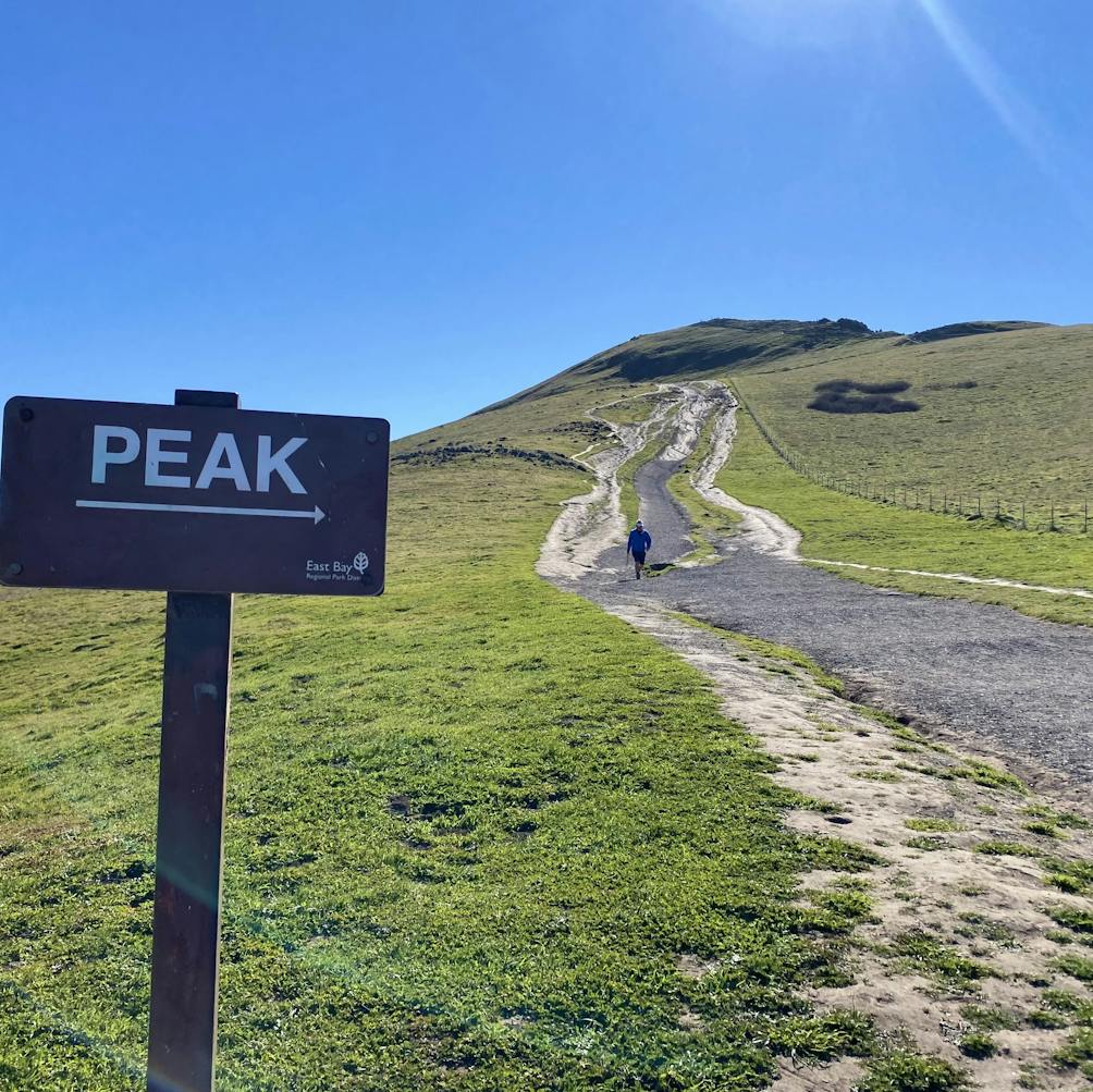 Sign for the peak of Mission Peak in the East Bay and a hiker on the trail 