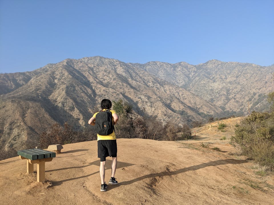 Hiker walking past a bench on a trail highpoint overlooking mountains in Hillside Wilderness Preserve in Monrovia 