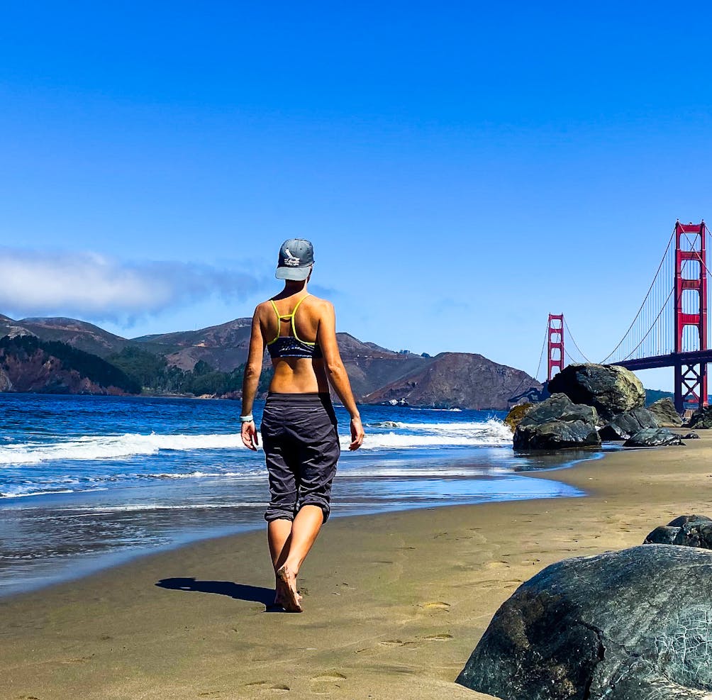 Person in bare feet walking at Marshall Beach in San Francisco, with a view of the Golden Gate bridge 