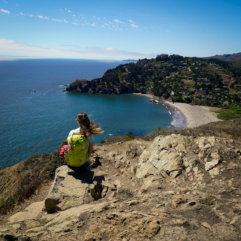 Woman sitting on a rock on the Coastal Trail and looking down below to Muir Beach in the Marin Headlands 