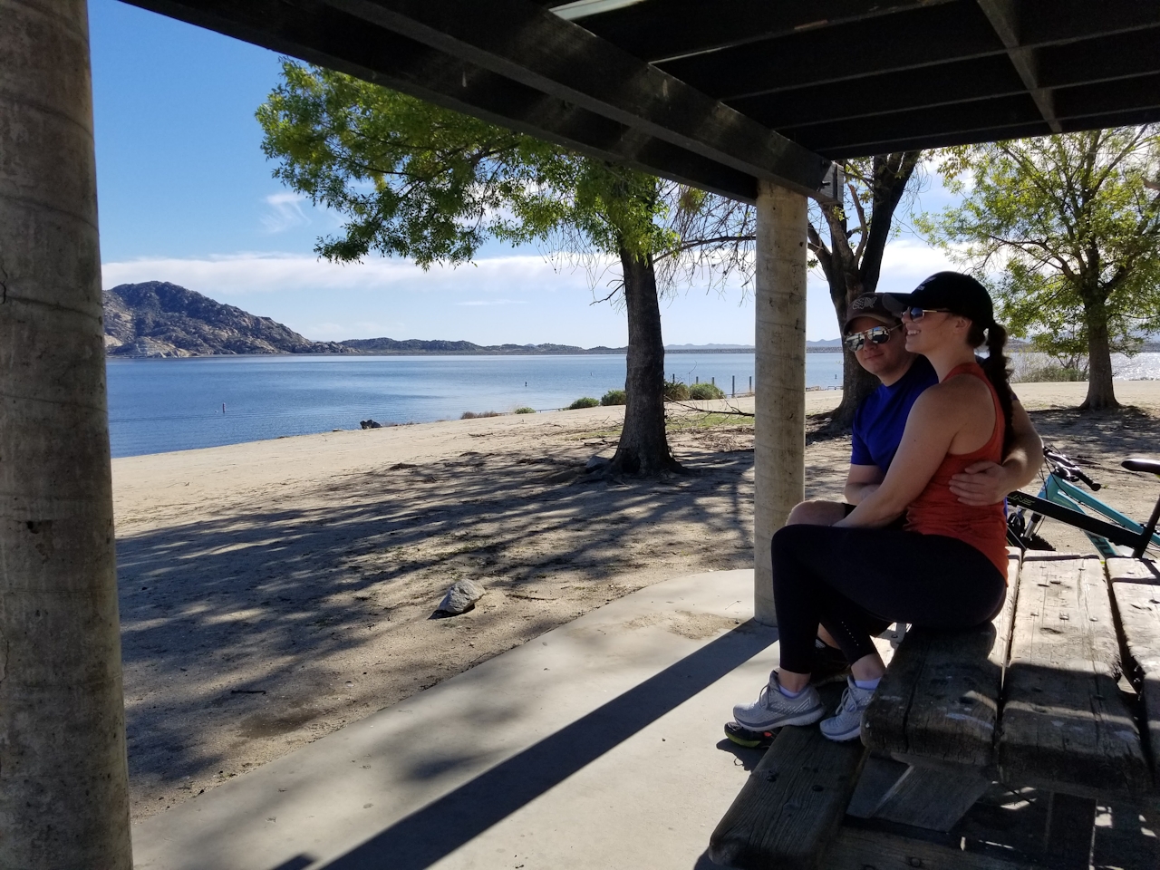 Two people at a picnic table overlooking a beach at Lake Perris State Recreational Area in the Inland Empire 