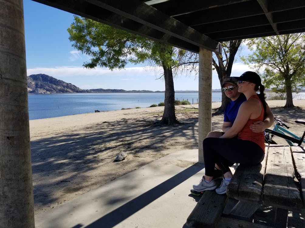 Two people at a picnic table overlooking a beach at Lake Perris State Recreational Area in the Inland Empire 