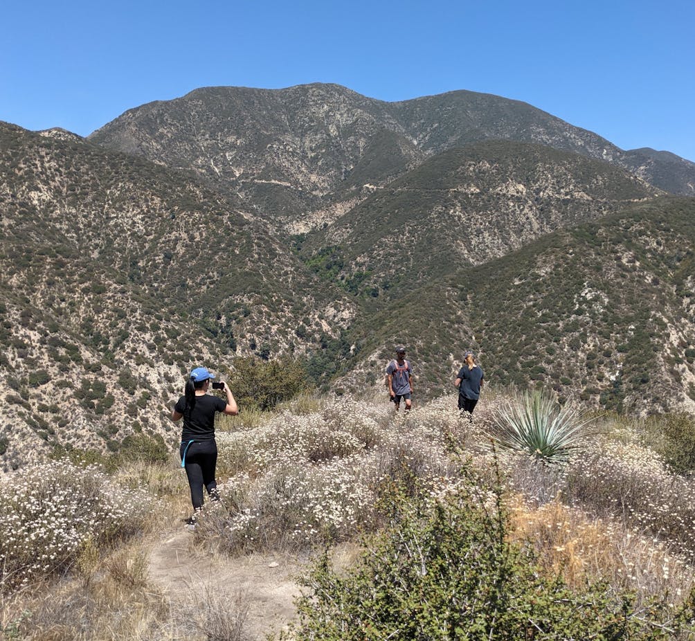 Woman taking a photo of friends ahead on a hiking trail in a canyon in Angeles National Forest 