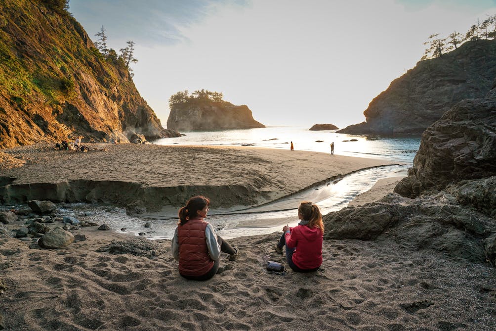 Two people sitting on the beach overlooking the estuary and ocean at Secret Beach on the Oregon Coast 