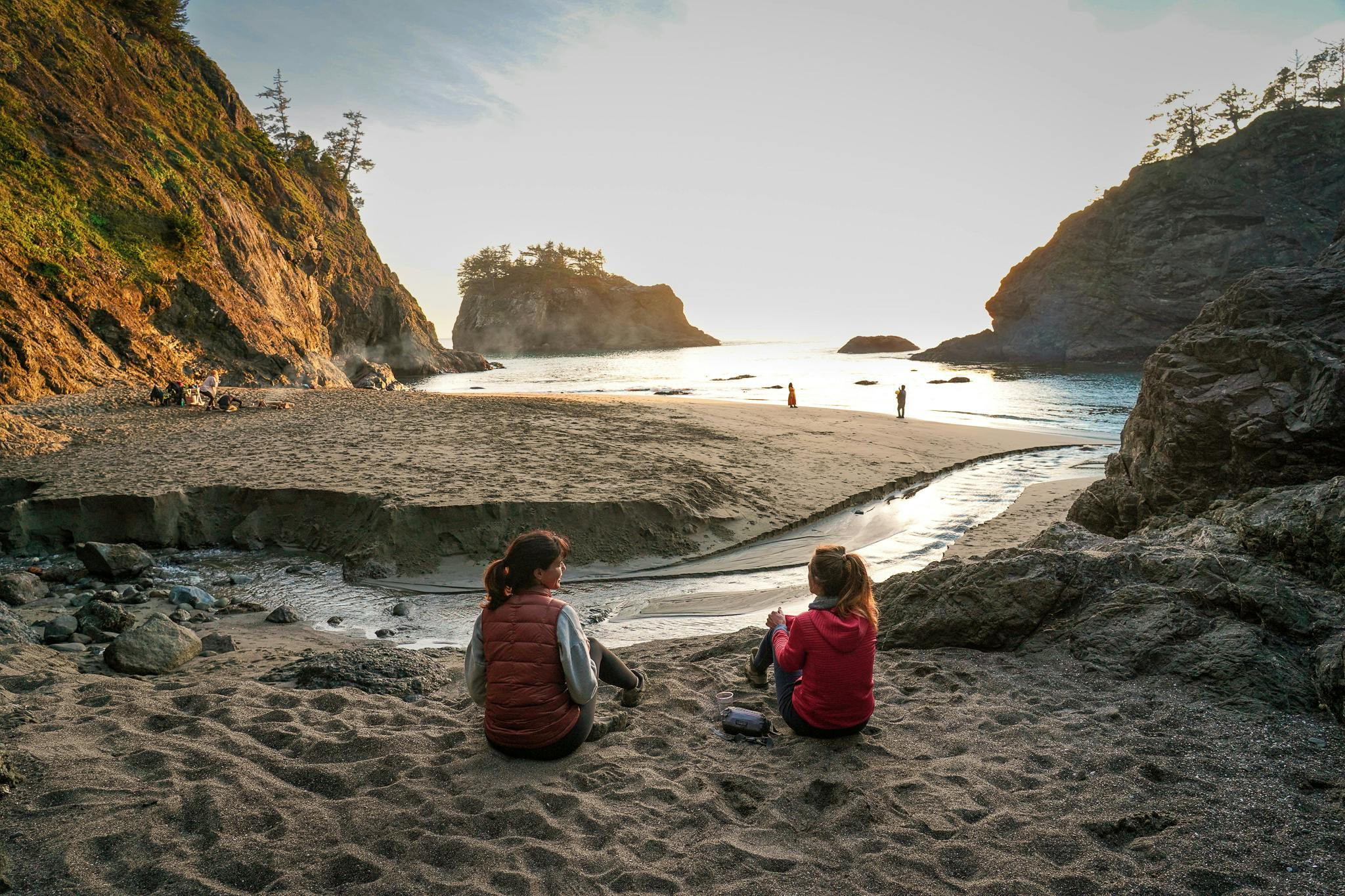 Two people sitting on the beach overlooking the estuary and ocean at Secret Beach on the Oregon Coast 