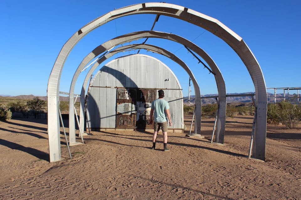 Person standing under giant arcing art sculpture at Noah Purifoy Desert Museum near Joshua Tree