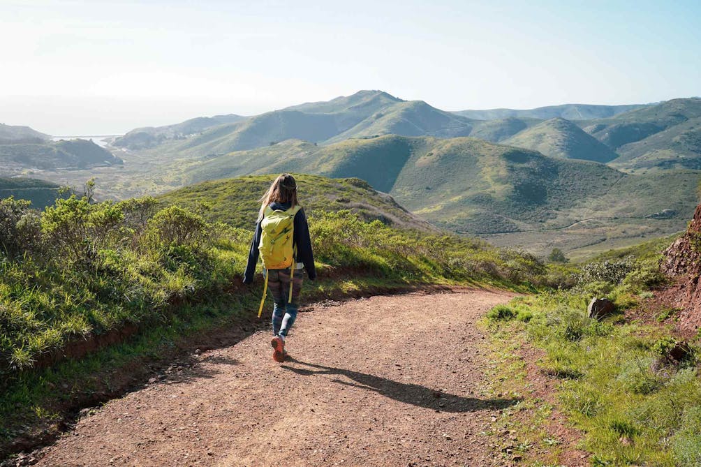 Hiker in front of rolling spring green hills on the SCA Trail in the Marin Headlands 