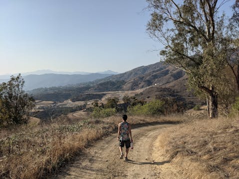 Hiker along a wide trail overlooking the San Gabriels at Horsethief Canyon in San Dimas 