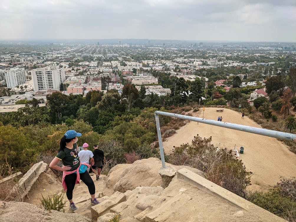 Hiker taking a break on stair steps and looking out to the city view of LA at Runyon Canyon in Los Angeles 