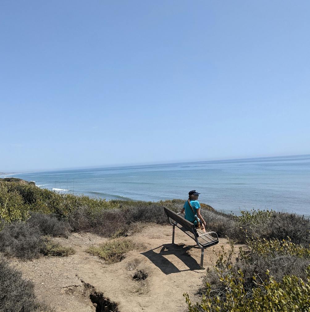 Woman sitting on a bluff top bench overlooking the Pacific ocean on the San Onofre Bluffs Loop Trail overlooking San Onofre State Beach in San Diego County 