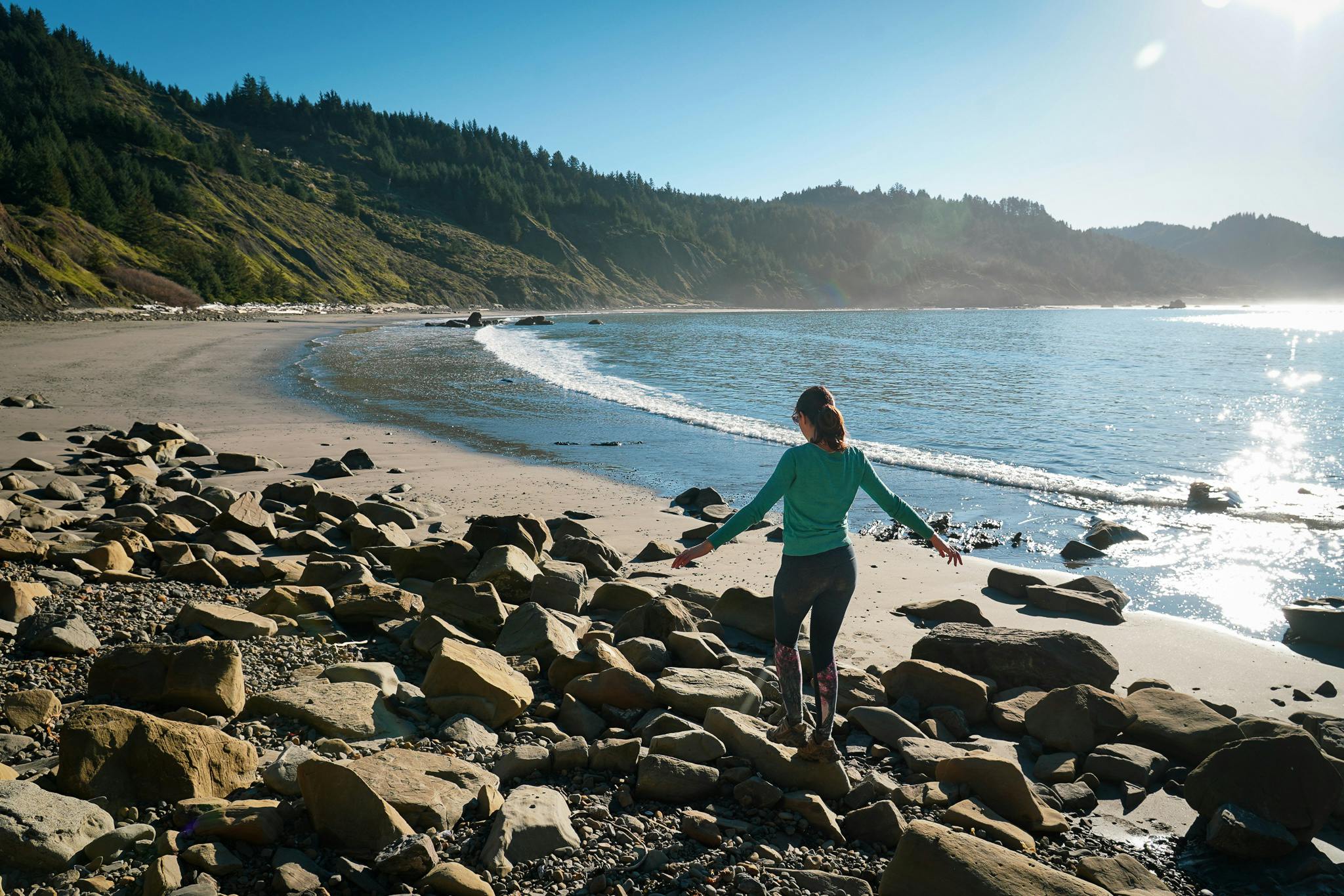 A woman crosses over some rocks at Hunters Cove hike-in beach at Cape Sebastian on the Oregon Coast