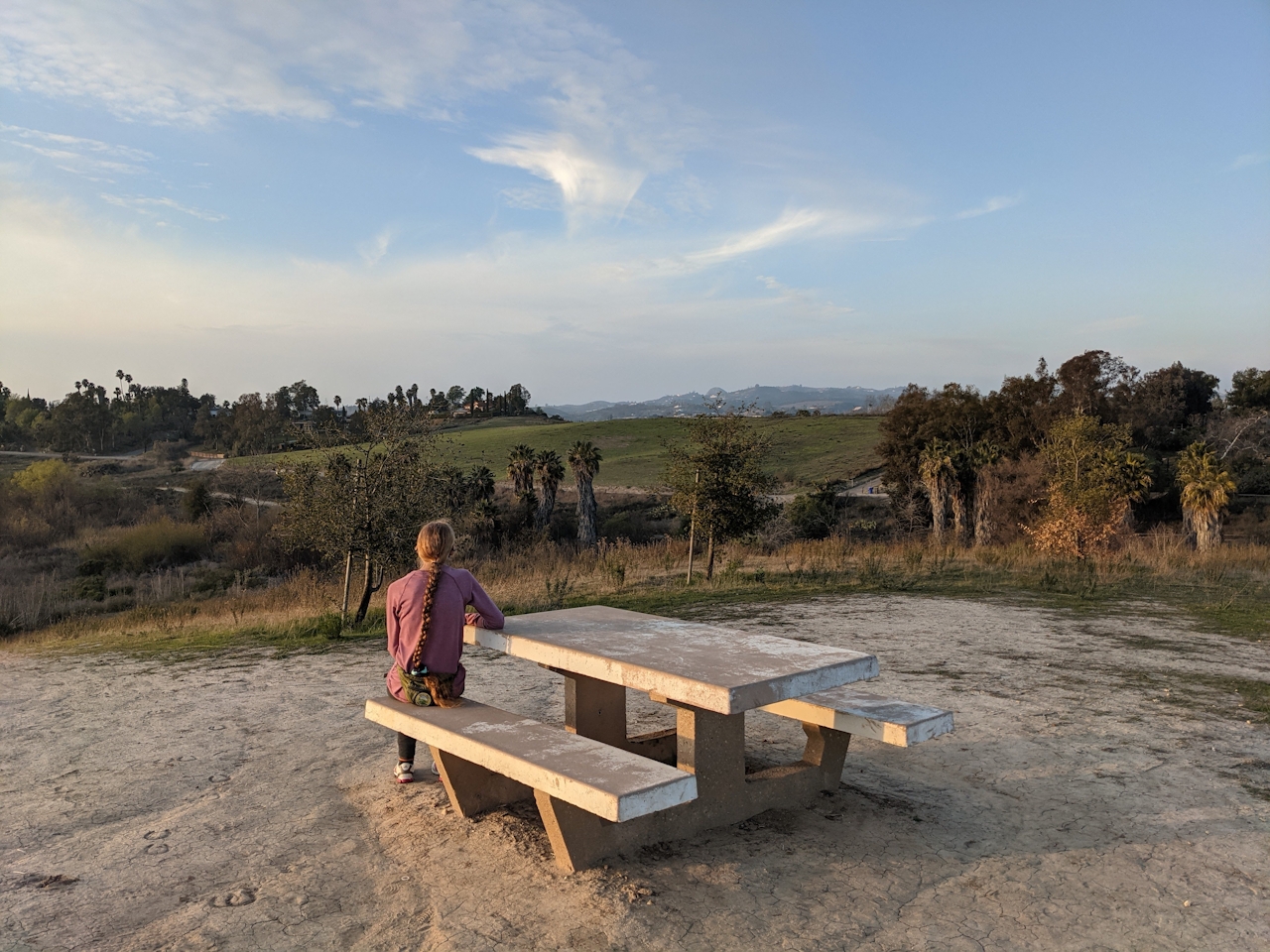 Woman sitting at a picnic table overlooking the trees and setting at Guajome County Park in San Diego 