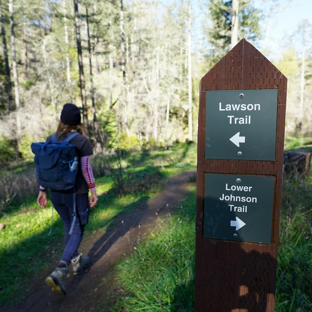 Woman hiking past signpost indicating the Lawson Trail in Hood Mountain Regional Park in Sonoma Valley