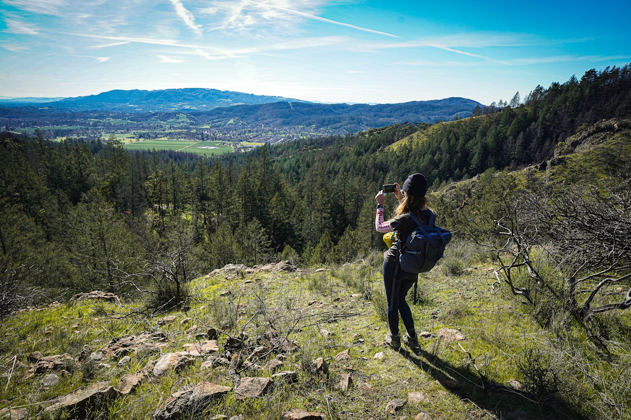 Woman taking a photo of the mountain to sea scenery atop the Lawson Picnic area at Hood Mountain Regional Park in Sonoma County 