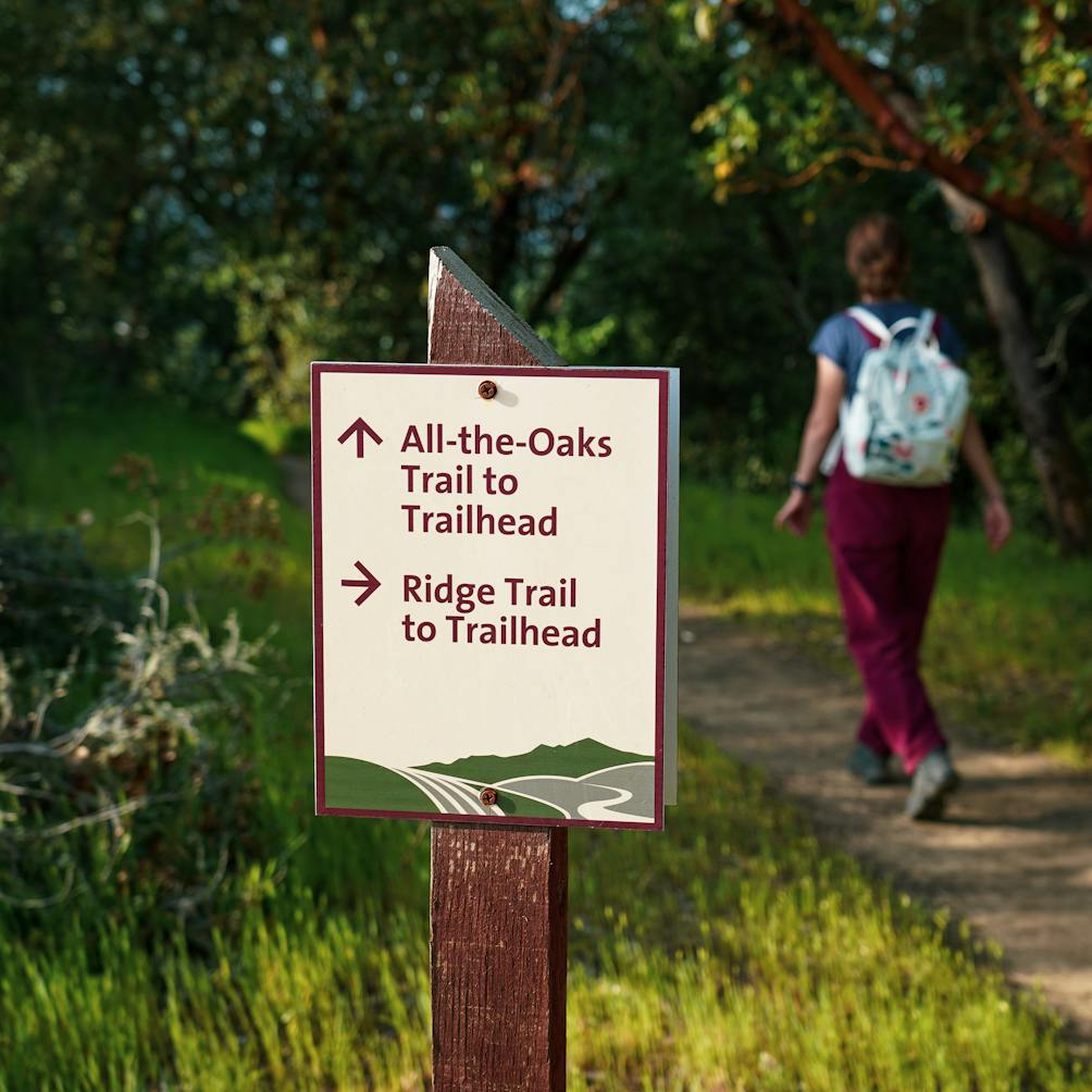 Hiker passing trail sign for All the Oaks Trail and Ridge Trail at Healdsburg Ridge Open Space 