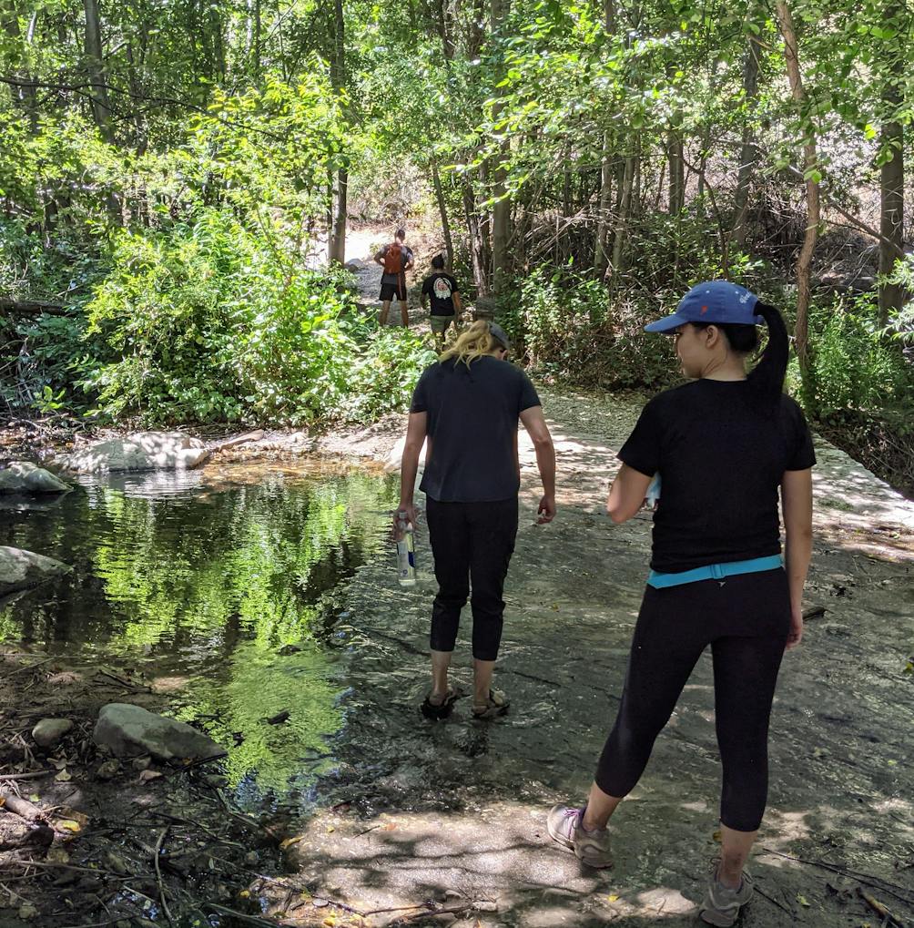 Two hikers walking through a small creek on a hiking trail in Angeles National Forest 