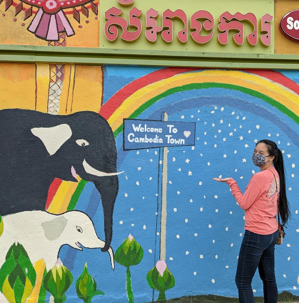 Woman standing at a mural welcoming here to Cambodia Town in Long Beach 