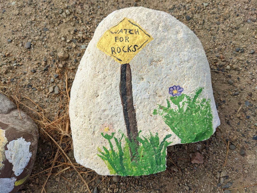 Rock with a sign painted on it saying Watch for Rocks at aLake Elsinore trail