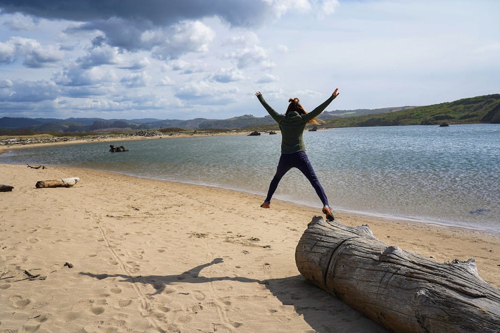 Woman leaping off a tree log by a lagoon at Pescadero Marsh Preserve