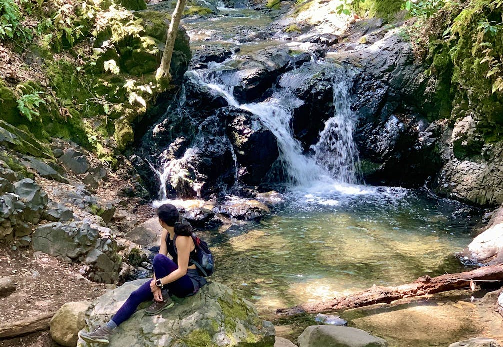 Woman sitting at the base of a waterfall at Uvas Canyon County Park in the Santa Cruz Mountains 