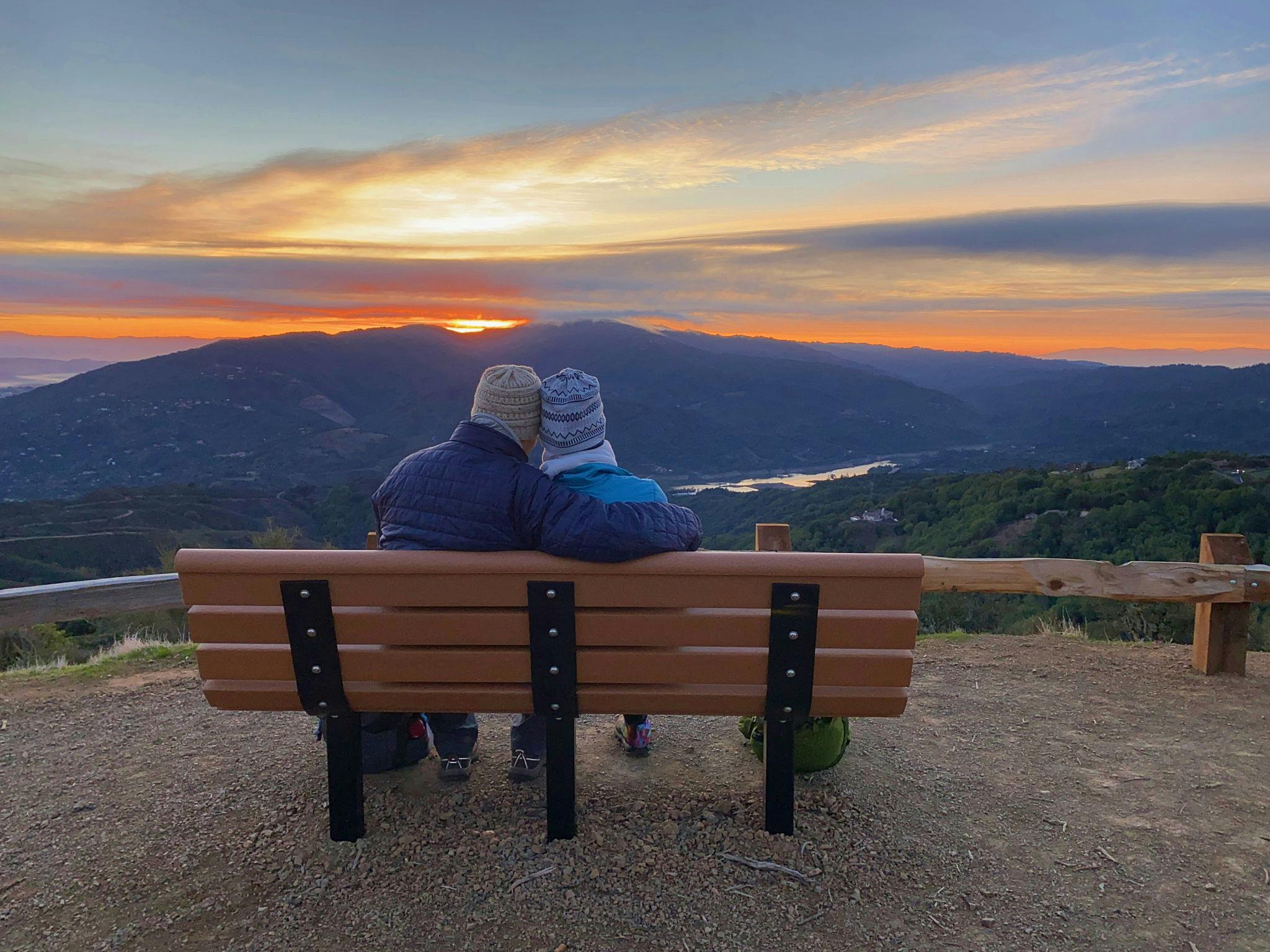 Couple sitting at a bench overlooking the Santa Cruz mountains at sunrise at El Sereno Preserve in the South Bay