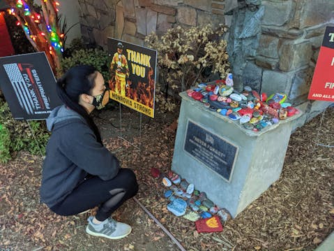 Woman kneeling down to look at an art rock tribute to firefighters in Monrovia