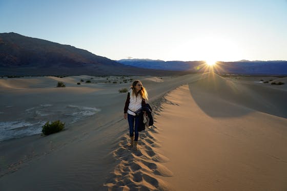 Woman standing on top of a sand dune at Mesquite Flat in Death Valley National Park at Sunset 