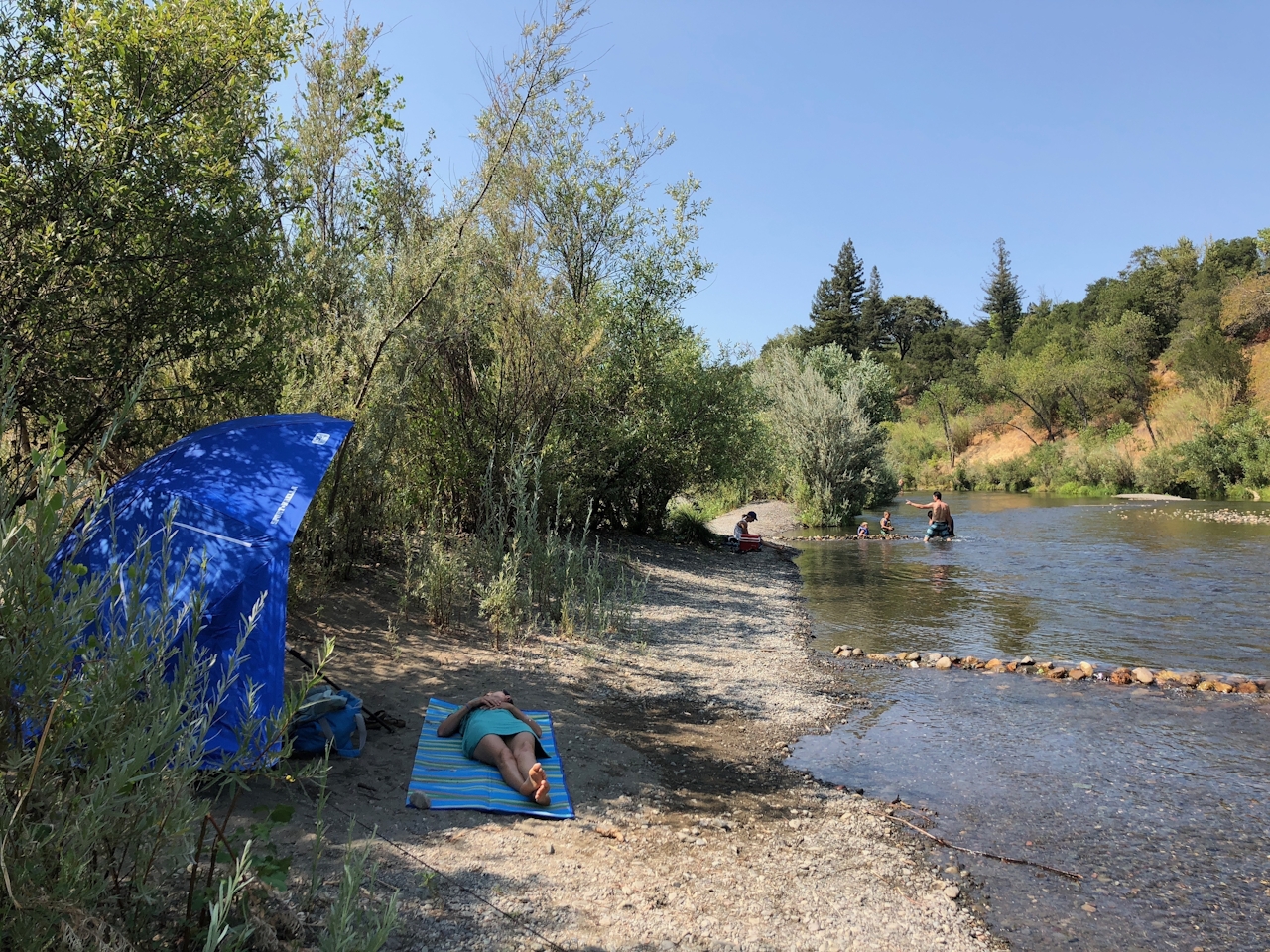 Woman lying on a towel beneath a sun umbrella at Del Rio Beach near Healdsburg in Sonoma County 