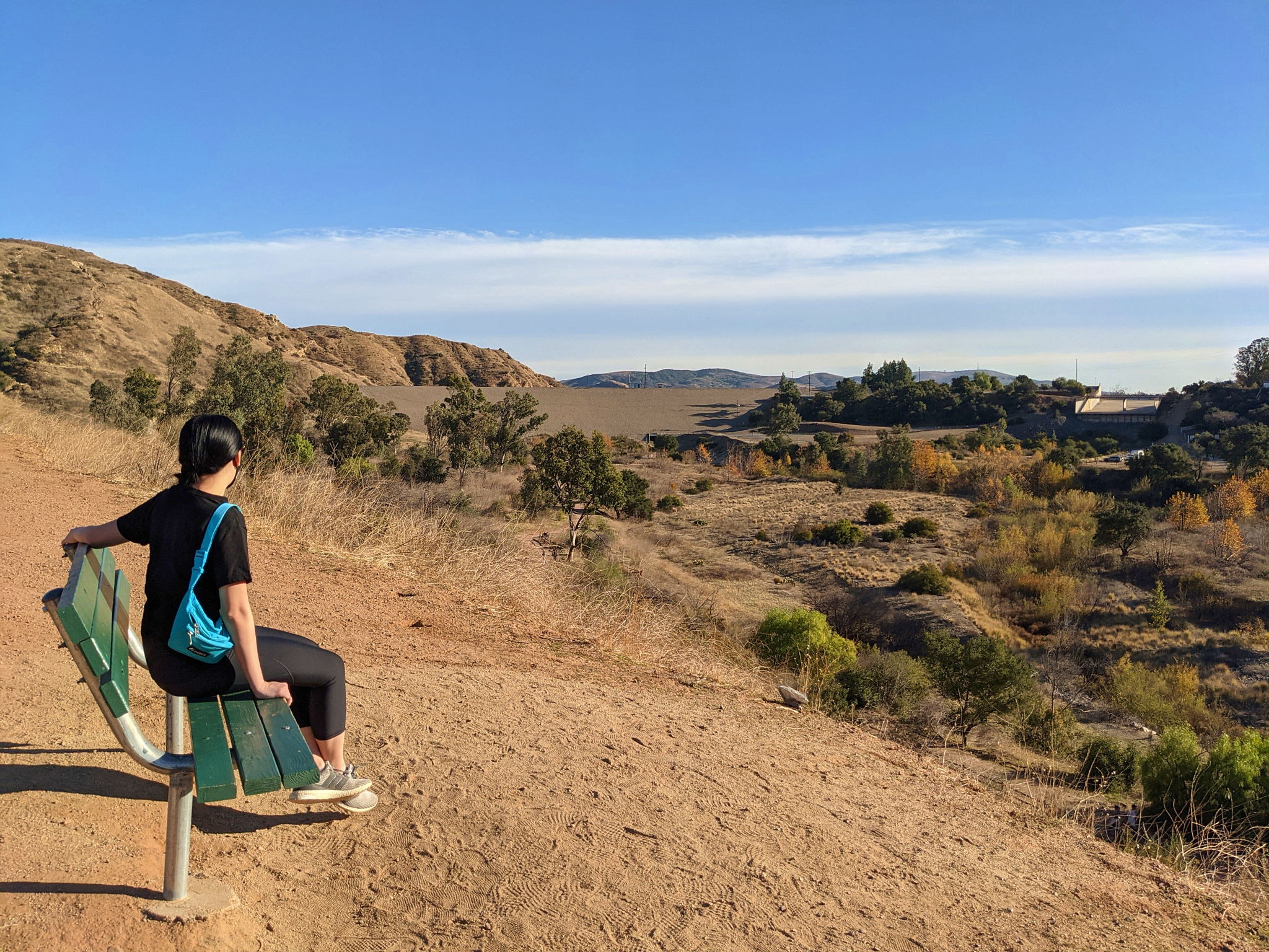 Woman sitting at a bench along a path overlooking Villa Park Dam at Santiago Oaks Regional Park