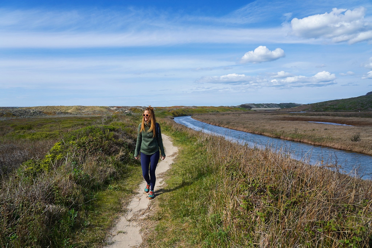 Woman walking the sandy trail next to the water at Pescadero Marsh Preserve