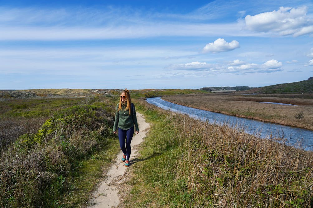 Woman walking the sandy trail next to the water at Pescadero Marsh Preserve