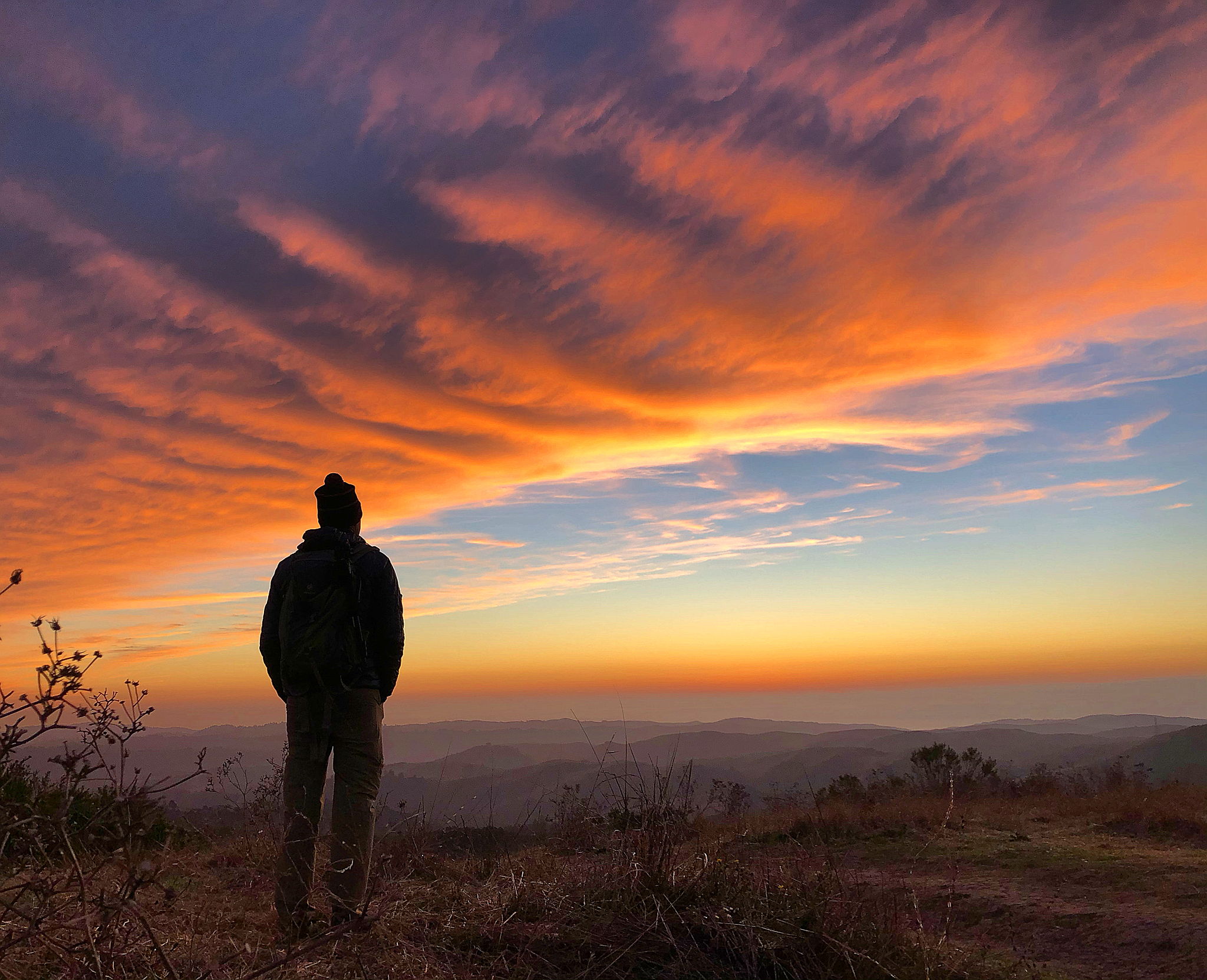 Man standing at Windy Hill and watching a fiery sunset at Windy Hill Preserve