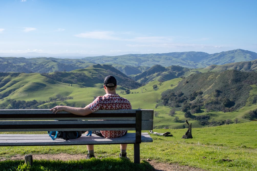 Person taking a hiking break sitting on a bench overlooking scenery at Sunol Wilderness Regional Preserve 