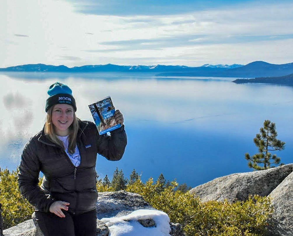 Nicole Szanto author of Tahoe & Reno guidebook, holding up her book in front of Lake Tahoe. 