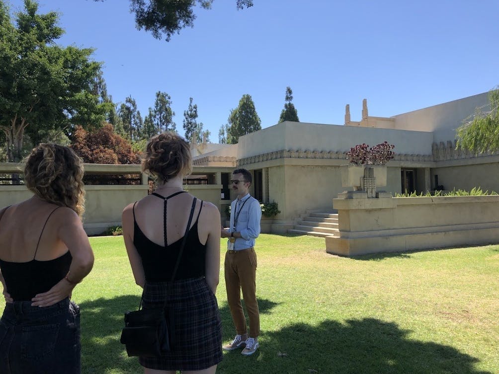 Two people taking a docent led tour of the outer grounds of Hollyhock House a Frank Lloyd Wright creation in Los Angeles