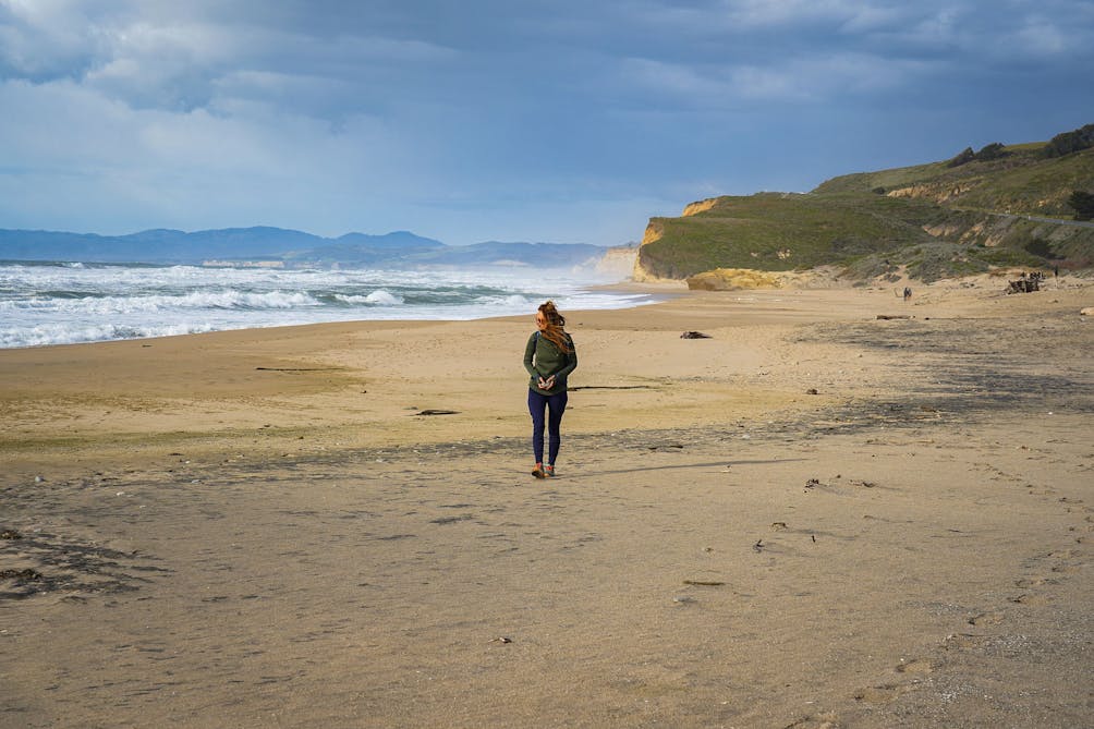 Woman walking along wide open Pescadero State Beach 
