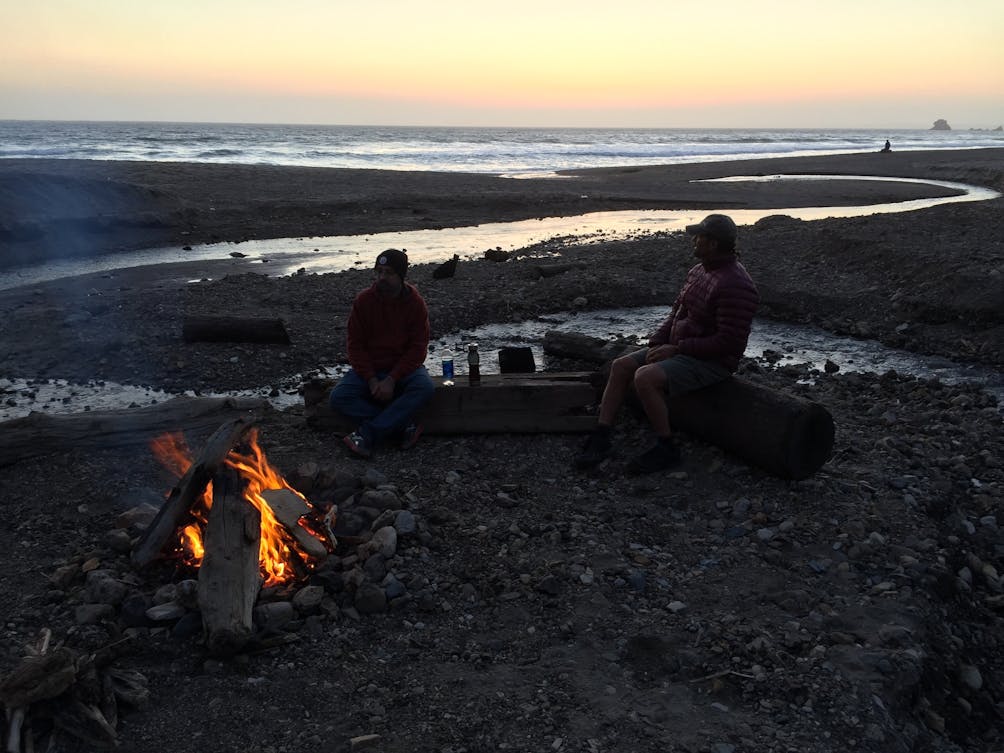 Two people sit around a campfire located at the beach near Wildcat Camp in Point Reyes National Seashore 
