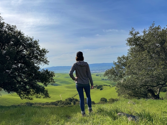 Woman standing at the top of Brush Peak in the East Bay Regional Park, looking out towards the mountain scenery