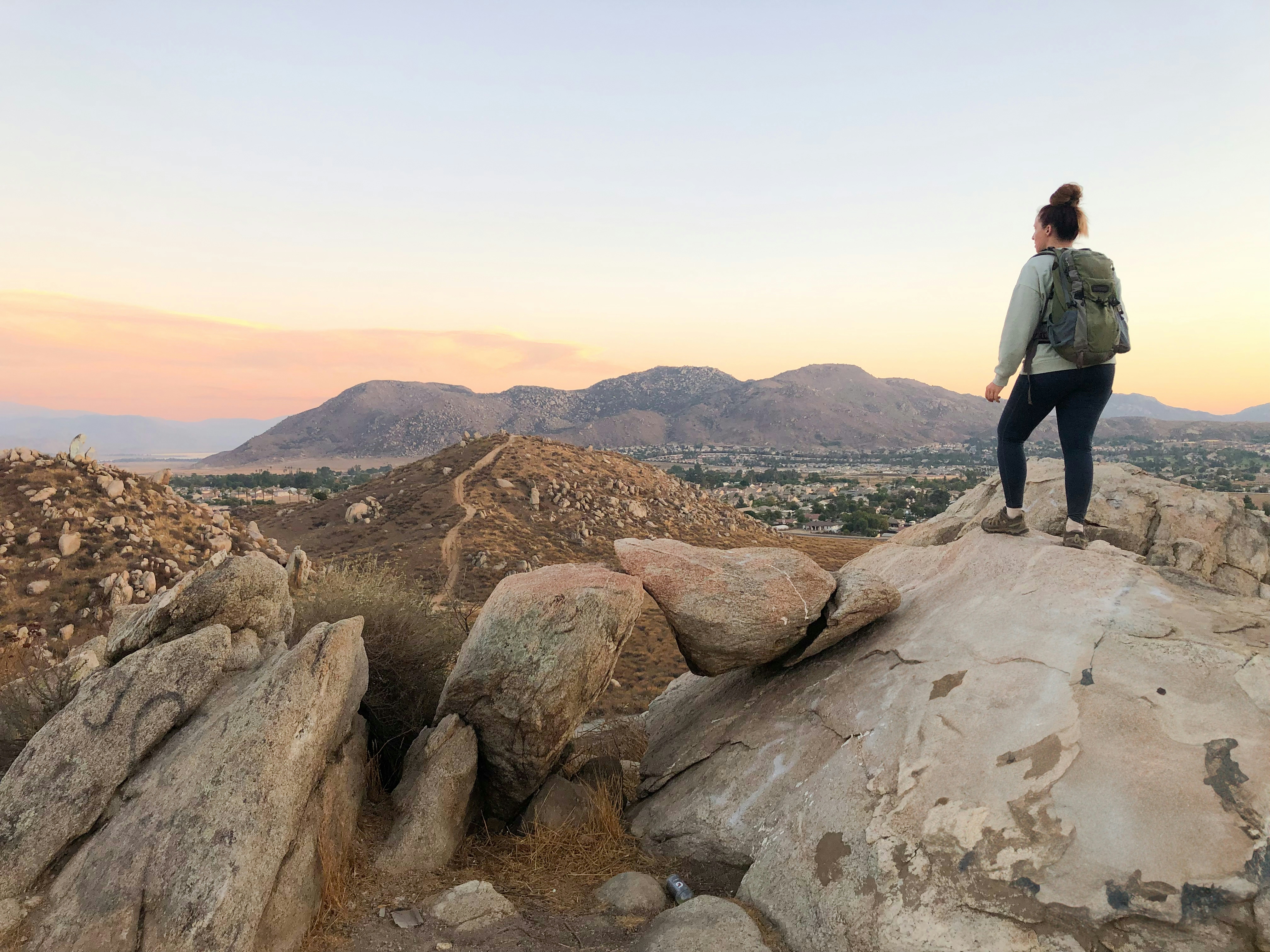Woman standing on rocks overlooking mountain scenery at sunset in Los Angeles County at Cold Creek Trail in Moreno Valley