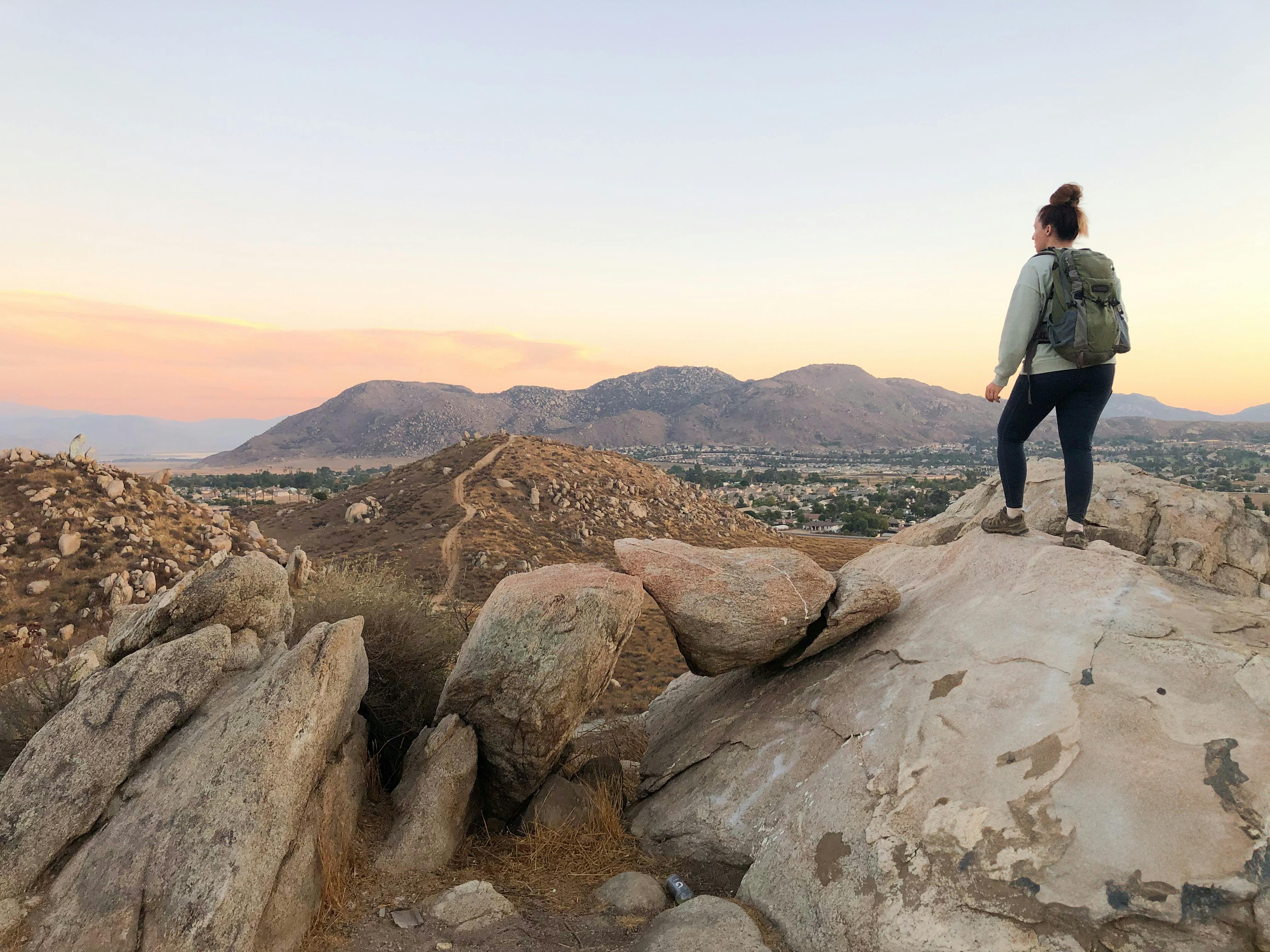 Woman standing on rocks overlooking mountain scenery at sunset in Los Angeles County at Cold Creek Trail in Moreno Valley 