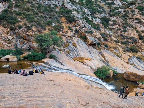 Hikers sitting on a large rock slab next to Three Sisters Falls in Cleveland National Forest Southern California near Julian 