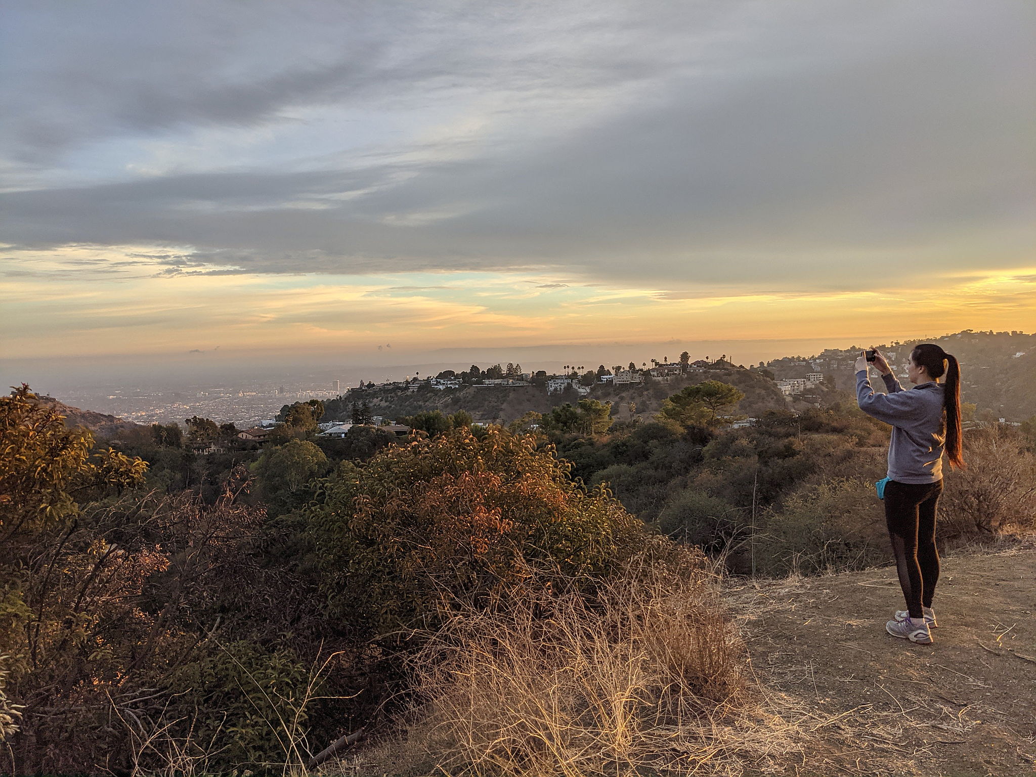 Woman standing and taking a phone photo of the view at Briar Summit Preserve in Los Angeles