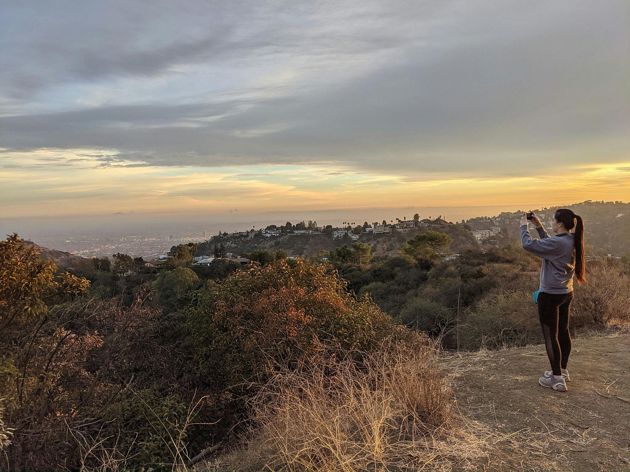 Woman standing and taking a phone photo of the view at Briar Summit Preserve in Los Angeles