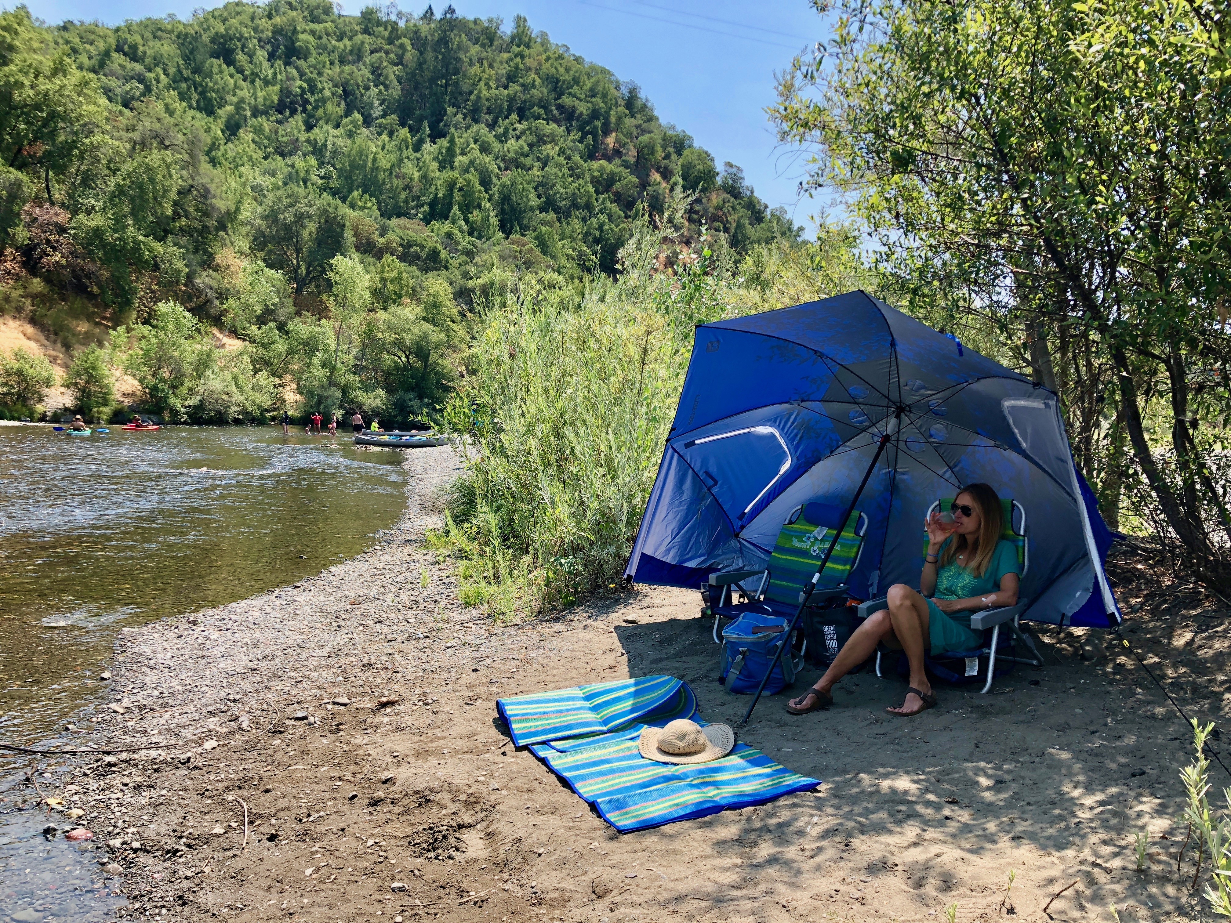 Woman sitting beachside under a sun umbrella at Del Rio Woods beach near Healdsburg in Sonoma County 