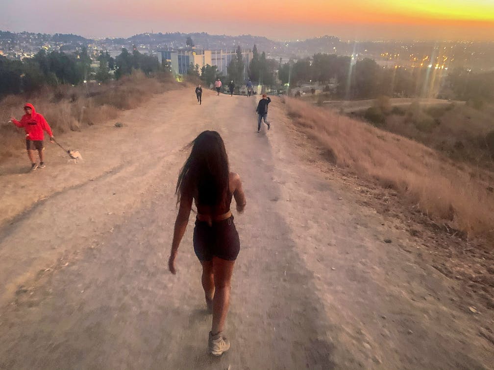 Woman hiking on wide trail overlooking downtown Los Angeles at Ascot Hills in Southern California 