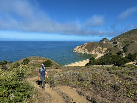 Man hiking up a trail at Montara Mountain, with a view of the Pacific and Grey Whale sand beach in the background