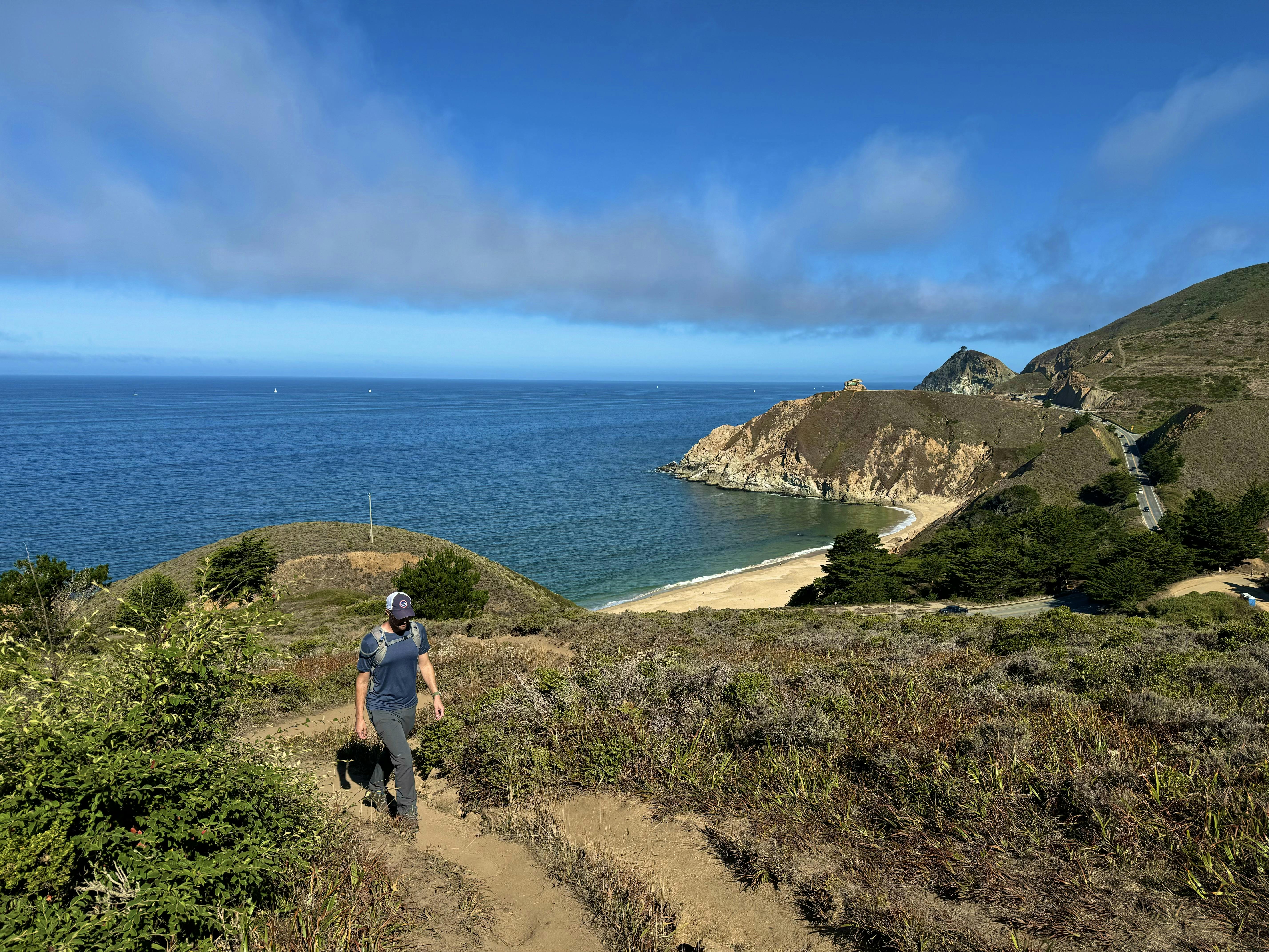 Man hiking up a trail at Montara Mountain, with a view of the Pacific and Grey Whale sand beach in the background