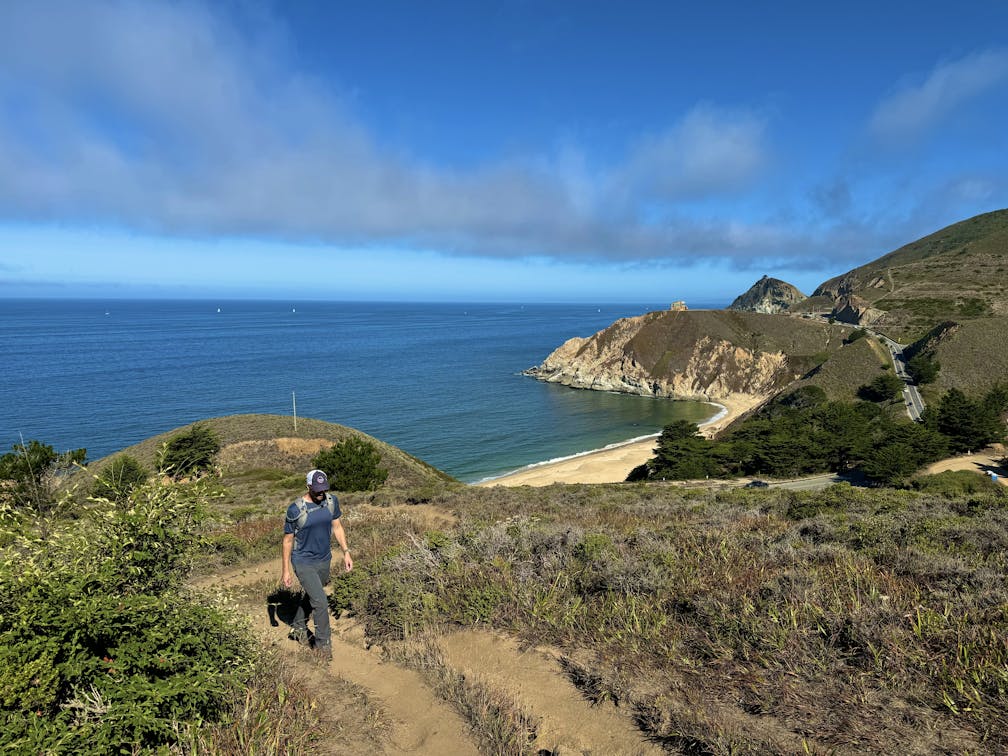 Man hiking up a trail at Montara Mountain, with a view of the Pacific and Grey Whale sand beach in the background