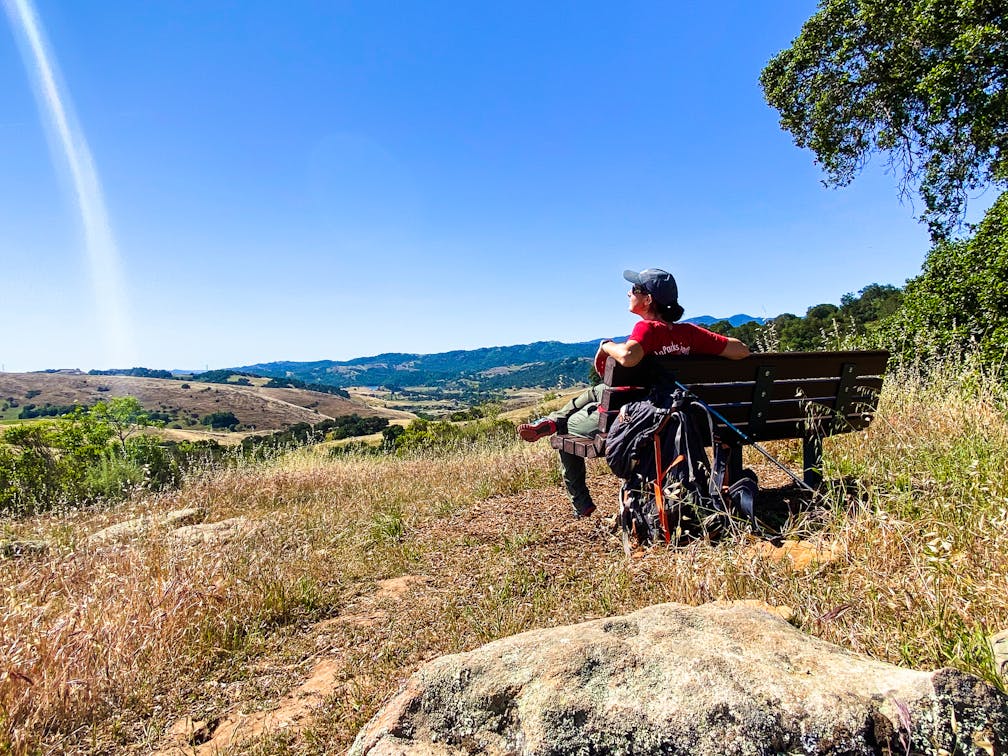 Hiker on a bench overlooking the vast scenery of mountains at Santa Teresa County Park in San Jose