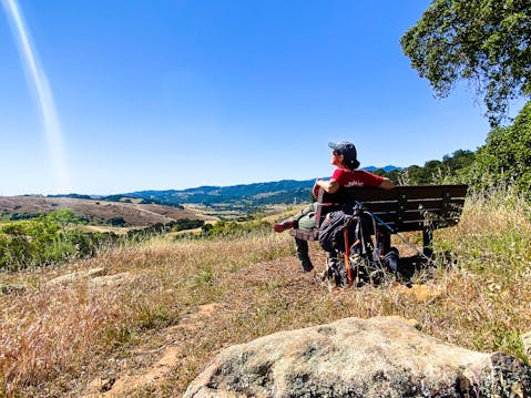 Hiker on a bench overlooking the vast scenery of mountains at Santa Teresa County Park in San Jose